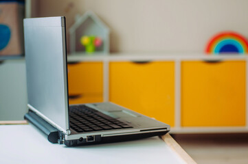 Laptop on the table in the childs room. Defocused interior of kids living room as a background. E-learning or virtual communication during stay at home quarantine.