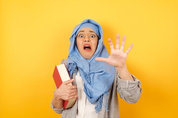 Young muslim woman wearing hijab frowns face, has disgusting expression, shows tongue, expresses...
