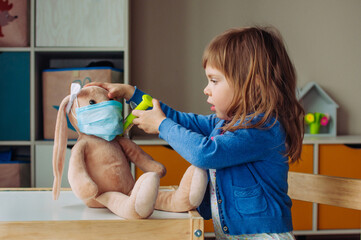 Toddler girl playing doctor giving an injection bunny toy