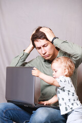 young man working at home with a laptop with a baby on his hands. Stay home concept. Home office with kids.