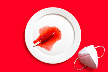 Delicious defrosted strawberry popsicles on white round dish and medical mask over red background