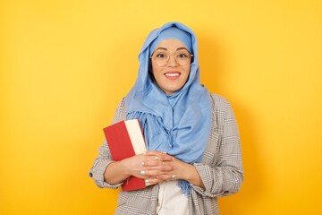 Wow. Beautiful muslim woman wearing hijab isolated on bright studio background. Young emotional surprised woman standing with open mouth. Human emotions, facial expression concept. Trendy colors.