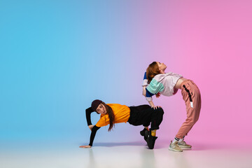 Flexible. Sportive girls dancing hip-hop in stylish clothes on colorful gradient background at dance hall in neon light. Youth culture, movement, style and fashion, action. Fashionable portrait.