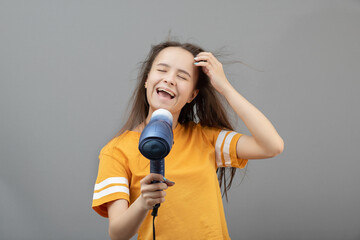 Young caucasian woman dries hair with a hairdryer on a gray background, has fun, sings like a microphone