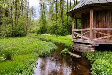 Wooden building (chapel) with porch at river bank. Architecture in water landscape. Szum river, Gorecko Koscielne, Poland, Europe.