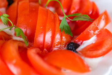 Red tomato cut into slices in cream sauce with olives and parsley leaves, selective focus. As backdrop for menus, cookbooks, advertisements and other culinary projects