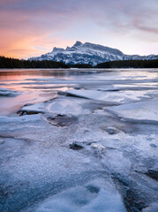 Colorful sunset on frozen lake with isolated mountain in background, shot during sunset at Two Jack Lake, Banff National Park, Alberta, Canada