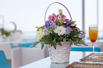 Alcoholic drink with fruit juice in glass and a basket of flowers, blur background
