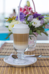 Latte in a glass with blurred background of a beautiful bouquet of flowers