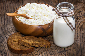 Fresh cottage cheese in a wooden plate with milk in a glass bottles