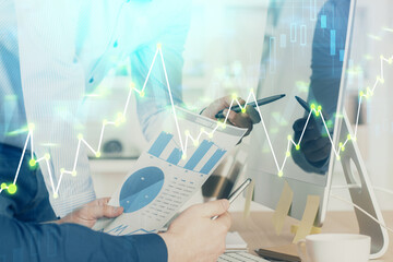 Double exposure of chart with businessman typing on computer in office on background. Concept of...