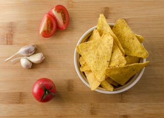 close-up of nachos with cherry tomatoes, garlic and spices on a light wooden background
