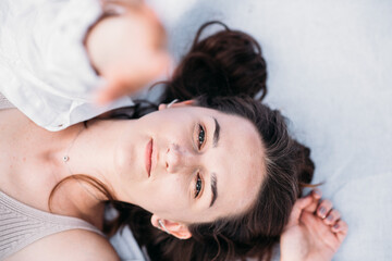 Portrait of a young woman with natural makeup, looking into the camera. Dressed in a white shirt. The woman lies on a white background. reaches for the photo camera