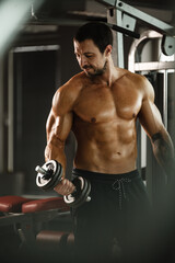Fototapeta na wymiar Fitness in gym, sport and healthy lifestyle concept. Handsome athletic man with naked torso making exercises. Bodybuilder male model training biceps muscles with dumbbell