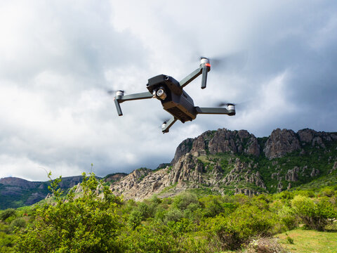 A gray drone quadrocopter with a camera flies in the mountains among the clouds.