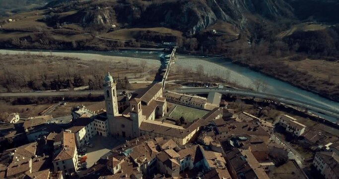 Aerial panoramic view of historical italian village inside the valley. Flying back from ancient church to the town. River flowing between mountain. Above old stone bridge panning rotation footage