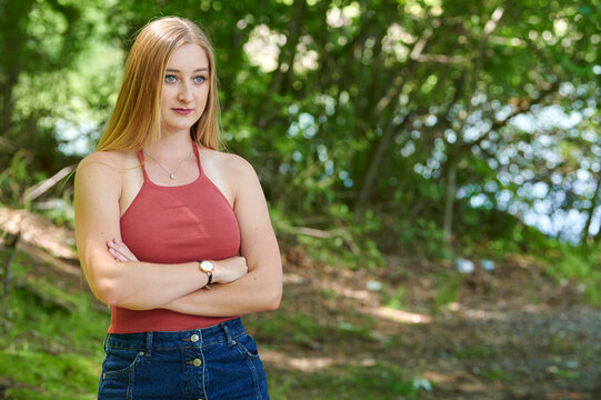 Beautiful young blonde woman posing for photo in woods wearing orange tank top and denim skirt - outdoors