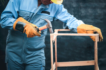 Worker wearing safety equipment, carpenter holding a hammer for repairing and maintenance, man with hammer hitting nails to fix some wooden furniture