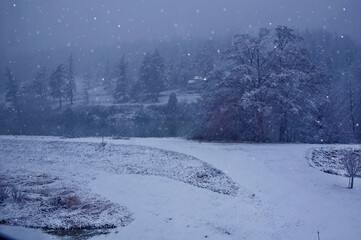This landscape is a snowstorm just starting up intensively in a country setting by a river.  Low lying clouds over the hill.