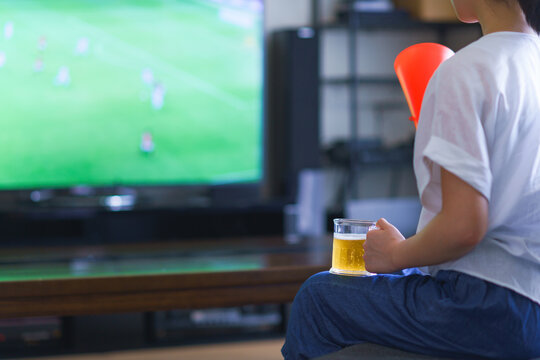 家でスポーツをテレビ観戦する若い女性のイメージ【プロサッカーの動画配信サービス】