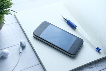  Close up of smart phone and pen on notepad on wooden table 