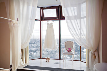 Details of the bride's morning. Wedding dress, bouquet and shoes by the big window
