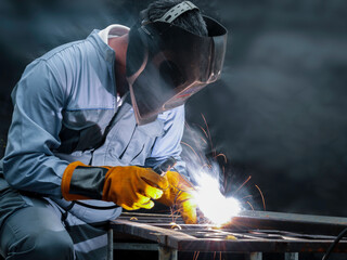 Industrial worker wearing safety mask, helmet, and safe glasses welding metal construction on factory. Industrial mechanic engineer working at the factory welding steel structure