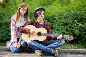 Fototapeta premium a pair of hipie boy and teen girl play guitar sitting on the sidewalk Asking For Money Donation