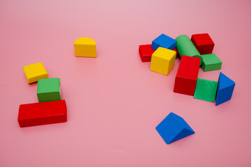 Colorful wooden blocks on pink background. Creativity toys. Children's building blocks. Geometric shapes - cube, triangular prism, cylinder. The concept of logical thinking.
