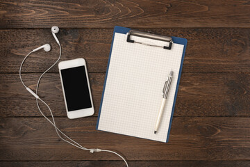Old wood office desk with smartphone, headphones and notepad. Top view with copy space