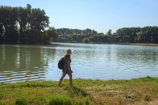 a young girl in a hat with a backpack on her shoulders walks along the shore on the lake, minimalism of travel
