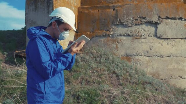 environmental pollution. man chemist scientist in a respirator mask studies landfill dump pollution radioactive waste disposal digital tablet and an white helmet stands next to standing radiation