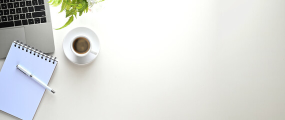 White working desk that surrounded by computer laptop, pen, note, potted plant and coffee cup.