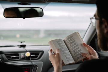 A man reads a book in a car during a long trip.