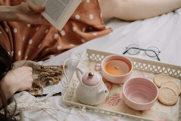 Woman reads a book at home in bed and drinks tea, home leisure in coziness and comfort.