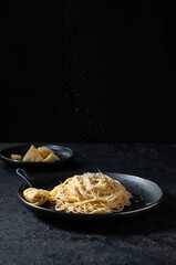 Cacio e Pepe - Italian Pasta with Cheese and Pepper on Black Plate on Dark Background