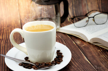 Close up of cup of coffee and eye glasses on book in background