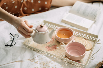 A woman pours hot tea from a teapot, home leisure in coziness and comfort.