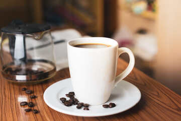 Cup of coffee with coffee beans and moka pot in background