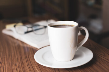 Cup of coffee with glasses and pen over book in background