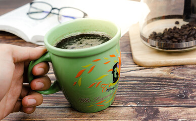Fototapeta na wymiar Hand holding green cup of black coffee on wooden texture