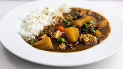 Japanese vermont curry vegetarian with tofu, peas, potatoes and chocolate over rice on white plate