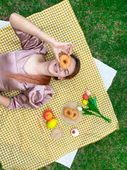 Close up  female asian lovely enjoying summer picnic ,Wearing romantic pink dress, Relaxed lying on the Yellow sheet Grid pattern, background green grass ,Fresh fruits and donut 