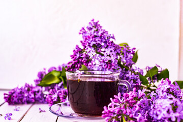 Cup of tea with lilac flowers on a wooden white background. Mocap for postcards. Spring time. Vase with lilacs. Copy space for text. The concept of holidays and good morning wishes
