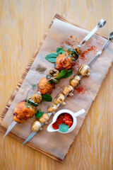 Fried  barbeque chicken on a skewer with potatoes and vegetables. Grilled BBQ decorated with vegetables and sauce on wooden table and parchment paper.