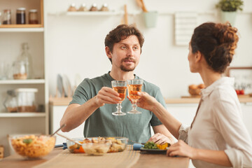 Young couple sitting at the table drinking wine and eating dinner in the domestic kitchen