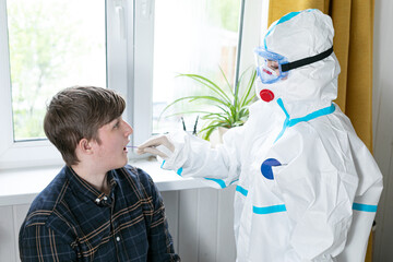 A man in a protective PPV suit against the Covid-19 virus. He takes a mason from the throat of a young man. Analysis is carried out at home. Nature. Quarantine Pandemic