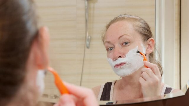 Portrait adult woman shaving face with razor. concept of hormonal disorders in women.