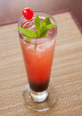 A delicious berry cocktail in a high glass with ice, cherry and mint garnish on a placemat in a restaurant.