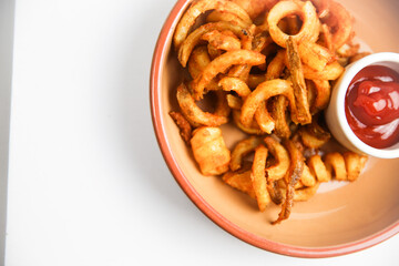 Curly fries on brown plate with white background side of ketchup
